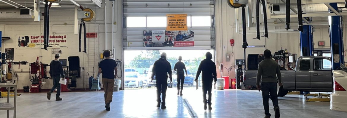 Cohort of 6 people in an automotive shop walking towards an open garage door