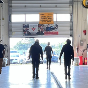 Cohort of 6 people in an automotive shop walking towards an open garage door