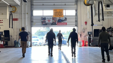 Cohort of 6 people in an automotive shop walking towards an open garage door